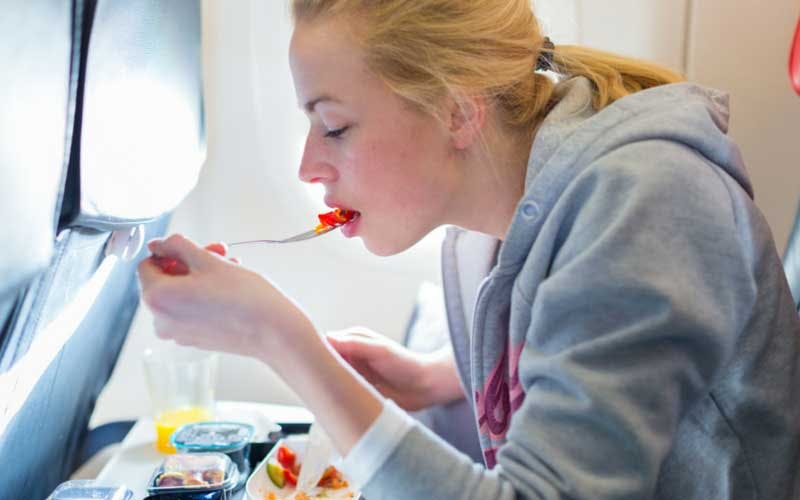 Girl eating meal on airplane.